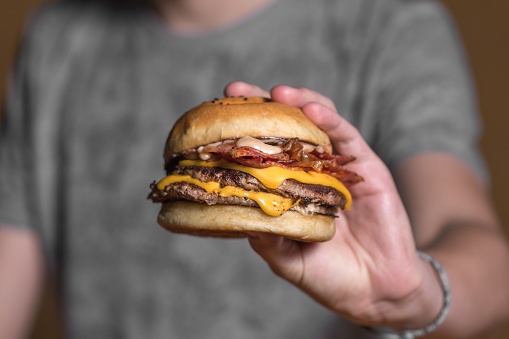 A closeup of a cheeseburger held by a man