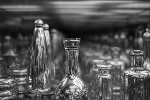 A grayscale shot of glass bottles and cups on an infinite mirror background