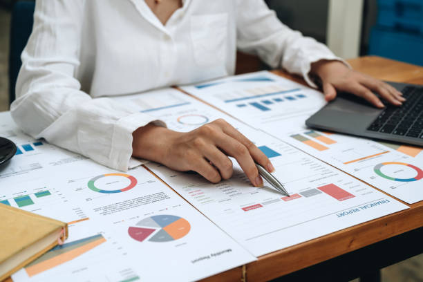 istock Business woman pen pointing turnover with graph chart report and use laptop computer for analysis data 1446626698