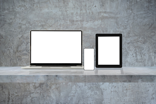 Laptop, mobile phone and digital tablet pc on grey wall shelf. Horizontal background.