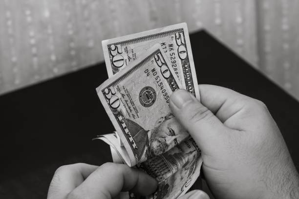 istock Grayscale closeup of person's hands holding and calculating stack of dollar banknotes 1446627710