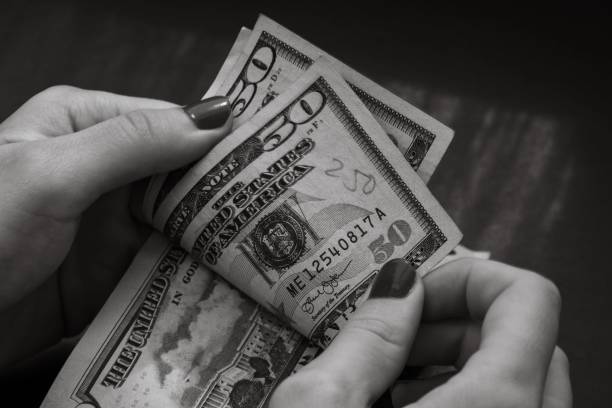 istock Grayscale closeup of person's hands holding and calculating stack of dollar banknotes 1446627712