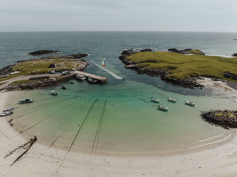 An aerial view of a kite surfer in water along Tiree island in Scotland with a sandy beach and seascape in the background
