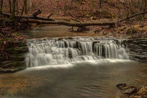 A autumn colors and fallen trees surrounding the beautiful Tanyard Creek Waterfall in Bella Vista, Arkansas,USA