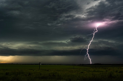 A beautiful shot of lightning strike in the night sky over a grassy field on a stormy night