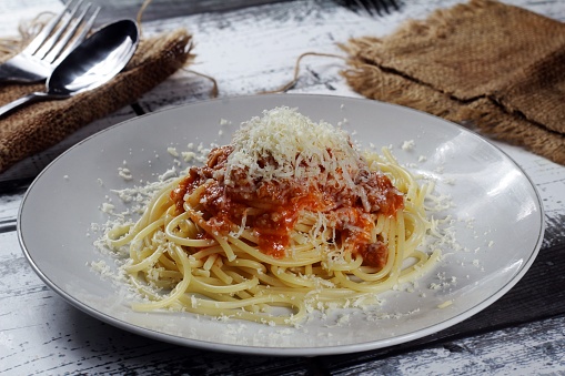 A closeup of a plate of spaghetti with meat sauce and \ngrated cheese on top