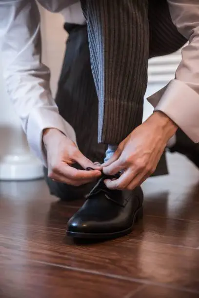 Photo of Vertical shot of man in classic outfit tying shoelaces