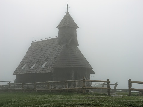 Wooden tower with the cross of the Church of the Mary of the snows on foggy day, Velika Planina, Slovenia