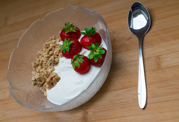 Bowl of dessert with white cream, walnuts, and strawberries on a wooden table with a spoon