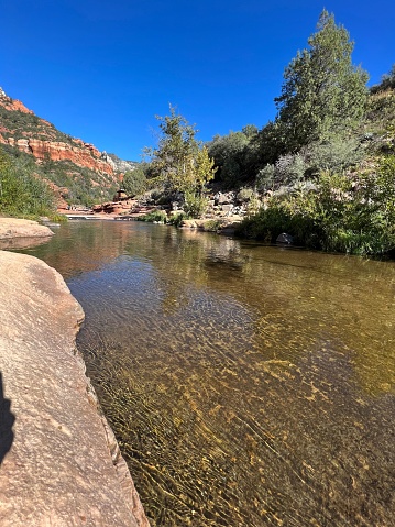 A river flowing through a ravine surrounded by red rock formations and trees at Slide Rock State Park