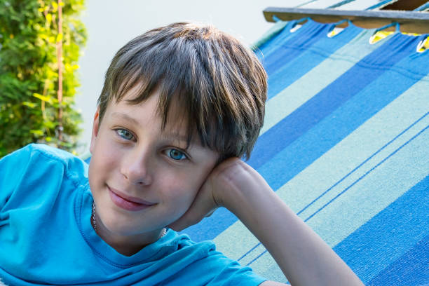 Face of a smiling boy close-up. Portrait of a 9-year-old boy in a blue t-shirt on a sunbed in the garden