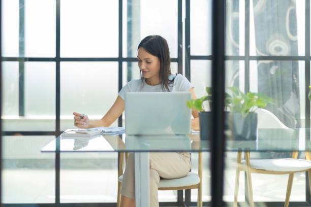 istock Beautiful caucasian business woman is working using digital tablet while sitting in creative office. The view is through the glass 1446645584