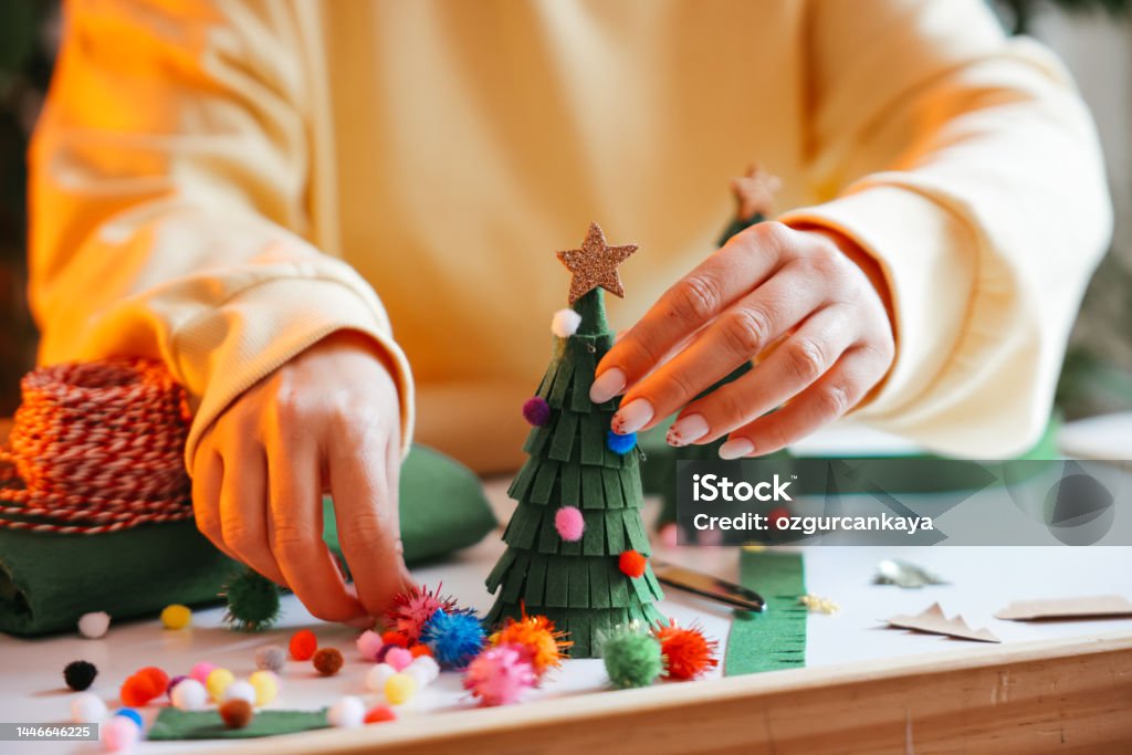 Woman wrapping Christmas gifts Young Woman Wrapping Christmas Gifts In Living Room. Creative diy craft hobby. Making handmade craft christmas ornaments and balls with felt spruce tree. Woman's leisure, holiday decorations. Closeup of female hands at white wood background Homemade Stock Photo