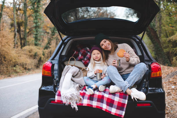 Mother with child daughter having picnic in car body Smiling woman eating biscuits with kid girl sitting in car body with blanket and decoration outdoor. Motherhood. northern europe family car stock pictures, royalty-free photos & images