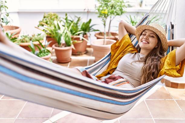 jovem hispânica usando chapéu de verão deitado na rede no terraço. - hammock comfortable lifestyles relaxation - fotografias e filmes do acervo