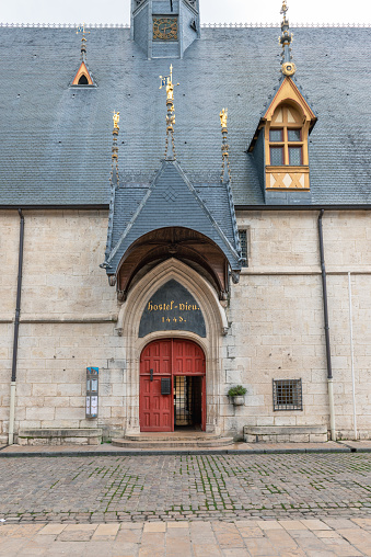 view of the entrance area of the Hôtel-Dieu. In the picture the red gate of the entrance, the entrance canopy and the dark roof with some gold-colored bay windows. The building of the former hospital now belongs to the hospices civils de Beaune and is a museum. The city of Beaune lies in the heart of the French wine-growing region of Burgundy, the city is surrounded by the vineyards of the Côte d'Or. 01/06/2022 - 2 Rue de l'Hôtel Dieu, 21200 Beaune, in the Côte-d'Or department in the Bourgogne-Franche-Comté region, France