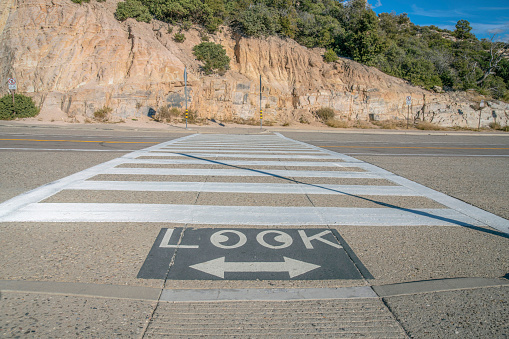 Mount Lemmon, Arizona- Crosswalk on a highway beside the rocky mountain wall. There is a painted warning on the pavement with LOOK word above the left and right arrow.