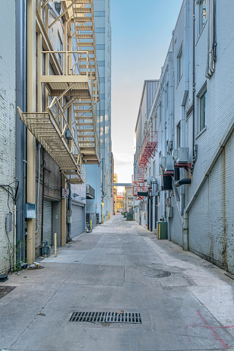 Austin, Texas- Concrete alleyway in between adjacent residential buildings. There are buildings on both side of the alley with emergency stairs and trash cans at the front.