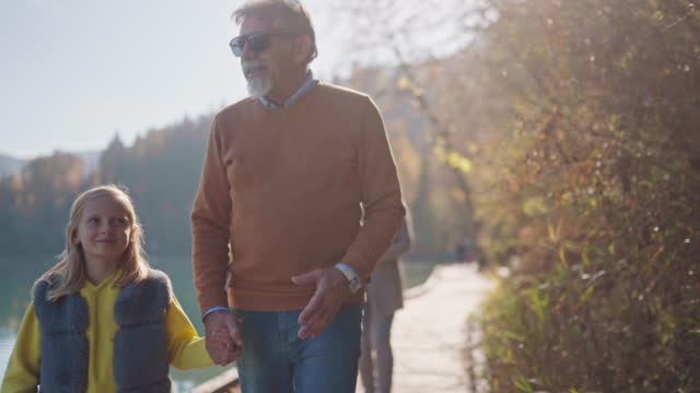 Loving Caucasian Grandfather And His Niece Holding Hands While Walking Around A Lake