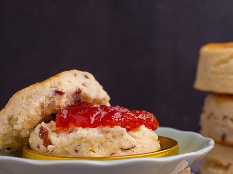 Traditional English style scones delicious freshly baked homemade with strawberry jam on a plate on a wooden table. Side view with copy space for text.