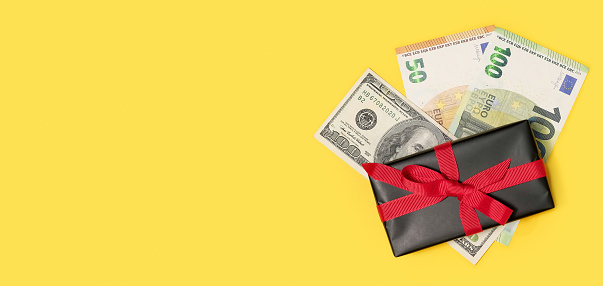 black gift box with a cash money on a yellow background. Festive background. Concept of presents, festive and holiday shopping. Holiday background