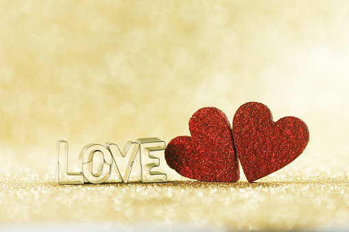 Two red glitter hearts and word love on golden bright glitter lights bokeh background