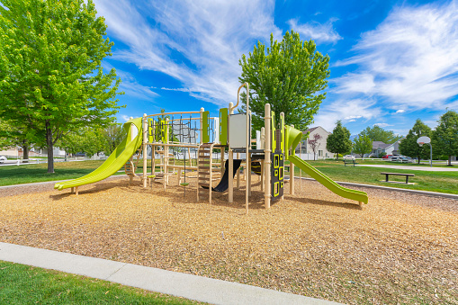 Playground set in a residential community at Utah valley. Playground in a public park with concrete path and basketball court at the back with benches on the side against the houses.