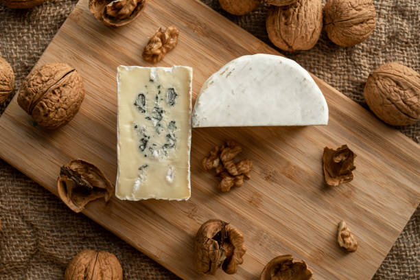 istock Composition of a cut cheese head with white and green mold and walnuts on a bamboo board on a background of burlap 1446672912