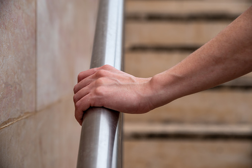 Woman hand using a railing to go upstairs with steps in the background