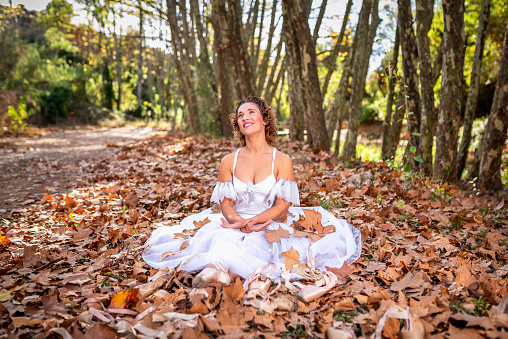 Mature ballerina sitting on the ground in autumn smiling surrounded by leaves