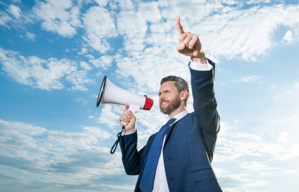 istock businessman shout in loudspeaker on sky background. point finger 1446683908