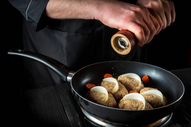 istock Cooking cutlets on pan by chef hands on black background for copy space text restaurant menu. The chef or cook adds pepper 1446687470