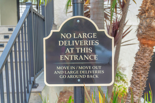 No large deliveries at the entrance signage at Carlsbad, San Diego, California. Instructions for large deliveries near the railings of a stairs on the left and trees at the background.