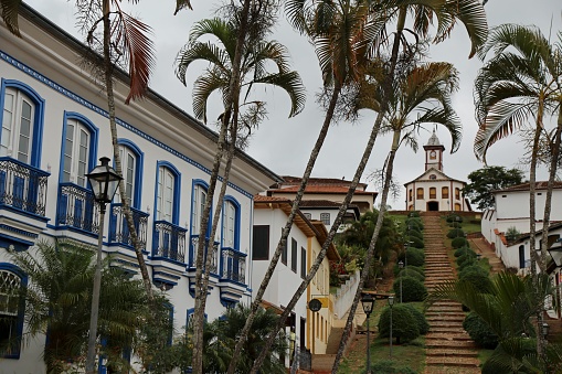 Colonial style buildings white and blue color. Palm trees and staircase and a church in the background.