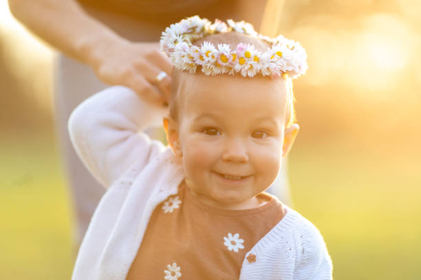 Young woman is playing with her baby girl in nature at sunset. They are beautiful and they are playing together