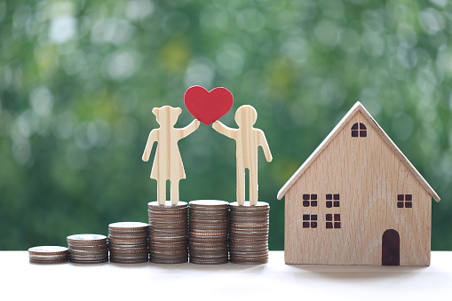 Love couple holding heart shape standing on stack of coins money with model house on natural green background, Saving for lover or family and save money for prepare in future concept