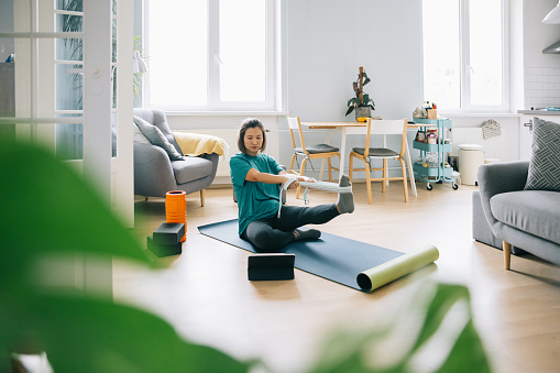 Mid adult Chinese woman doing yoga at home and using digital technological device