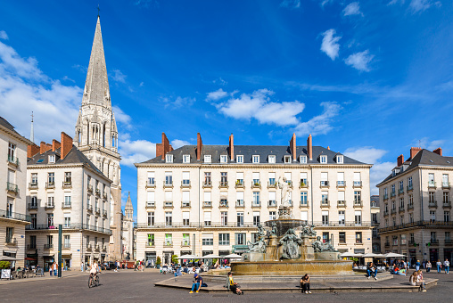 Nantes, France - September 16, 2022: The Place Royale pedestrian square with a monumental fountain, surrounded by classical-style buildings and overlooked by the steeple of St. Nicholas Basilica.