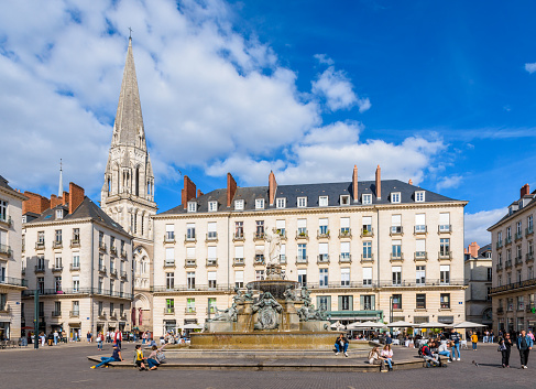 Nantes, France - September 16, 2022: The Place Royale pedestrian square with a monumental fountain, surrounded by classical-style buildings and overlooked by the steeple of St. Nicholas Basilica.