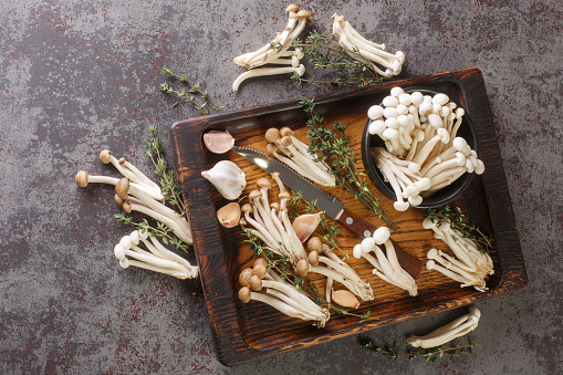 Edible raw white and brown beech mushrooms with thyme and garlic for cooking on a kitchen cutting board. horizontal top view