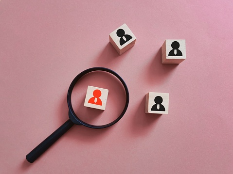 Head hunting concept on wooden cubes with magnifying glass against pink background.