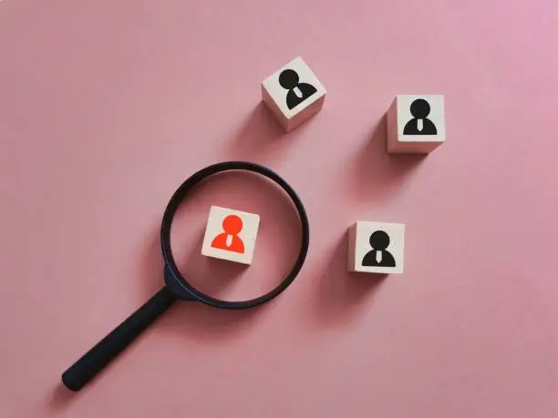 Photo of Head hunting concept on wooden cubes with magnifying glass against pink background.