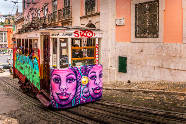 Lisbon, Portugal - December 04, 2024: Classic yellow tram on tracks on a city street. Buildings and shops line the street with people walking.