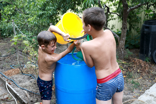 Two boys pour water on each other in backyard in summer