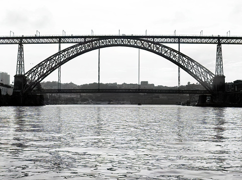 Black and white photo of Dom Lui¬s I Bridge day time, view from middle of Douro River, Porto, Portugal. Travel destination