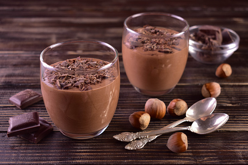 Mousse with dark chocolate with hazelnuts in glasses on a dark wooden background.