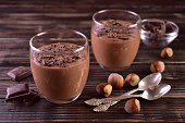 Mousse with dark chocolate with hazelnuts in glasses on a dark wooden background.