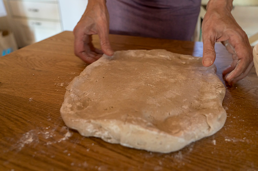 Elderly woman's hands kneading dough to make fresh bio italian pasta on marble table. Selective focus