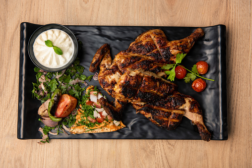 Full grilled chicken with mayo dip and salad served in dish isolated on table top view of arabian food
