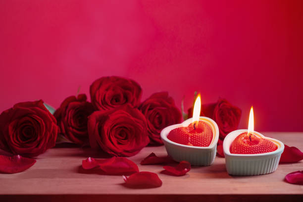 red roses with burning candles on pink background stock photo